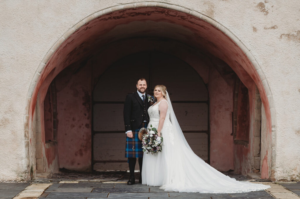 Aberdeenshire couple photographed by Aberdeenshire wedding photographer under iconic stable Arches at Meldrum House