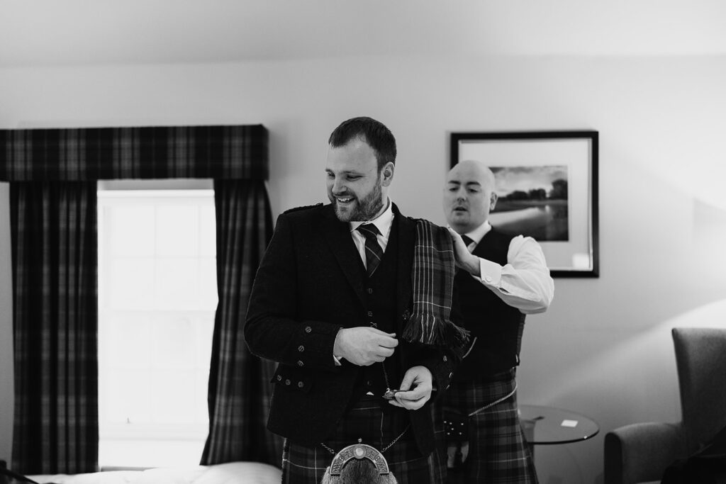 groom has jacket fixed by groomsmen at stables room at Meldrum House