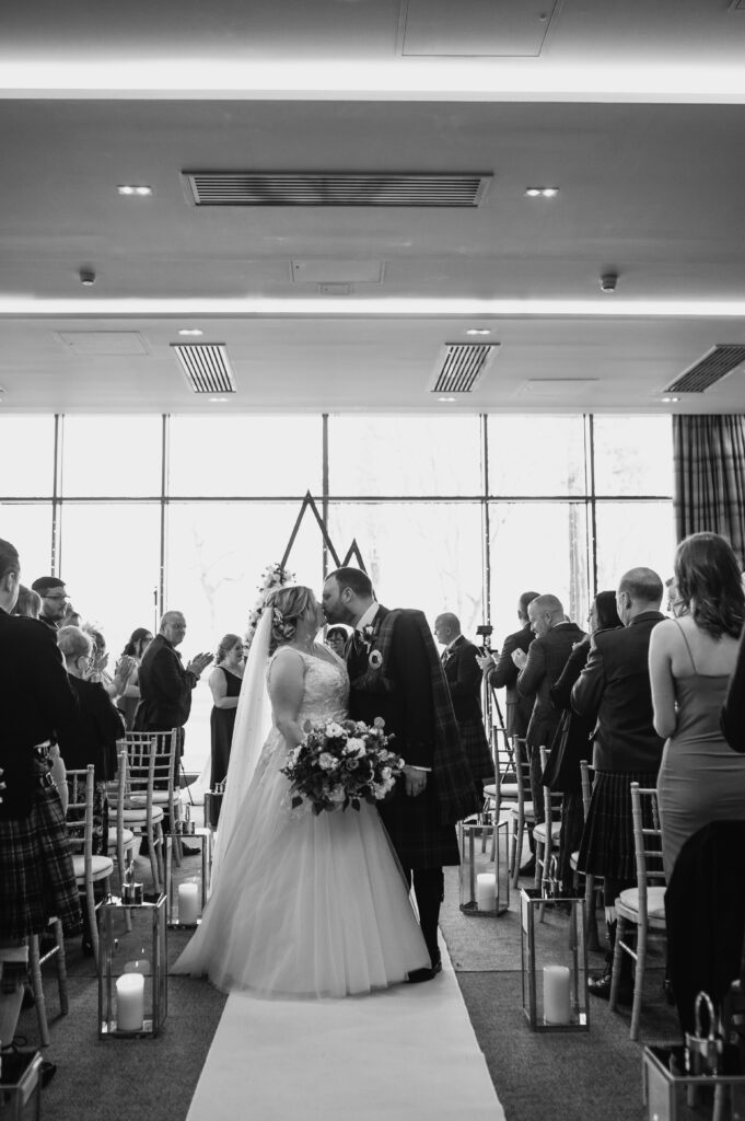 Aberdeenshire bride and groom share kiss down aisle at meldrum house, aberdeenshire 