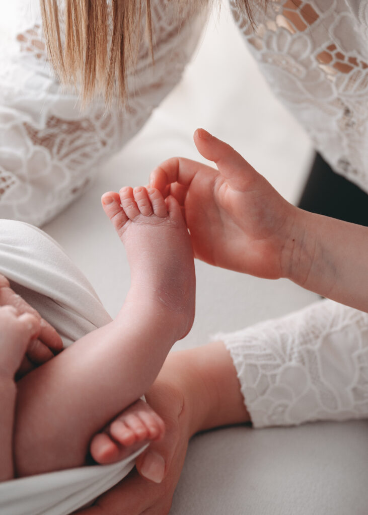 Sister holds feet of newborn sibling during newborn session in Aberdeenshire