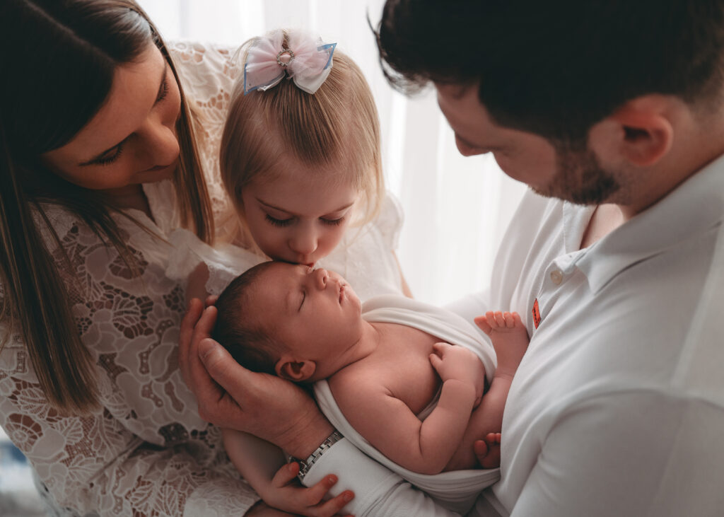 Sister kisses newborn sibling during newborn session in Aberdeenshire
