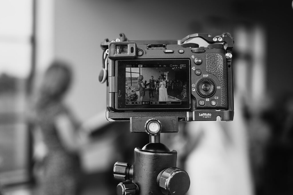 A professional camera on a tripod captures a wedding ceremony in sharp focus, with the couple visible on the screen - behind-the-scenes of Aberdeenshire wedding photography by Samantha Clyne.